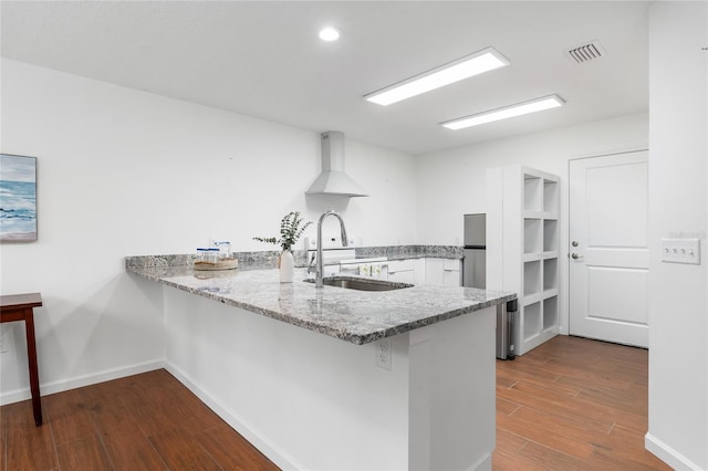 kitchen with white cabinetry, sink, kitchen peninsula, dark wood-type flooring, and wall chimney exhaust hood