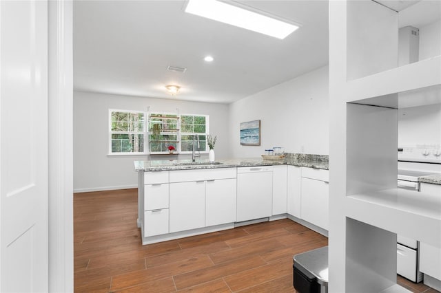 kitchen featuring dishwasher, sink, white cabinets, light stone counters, and kitchen peninsula