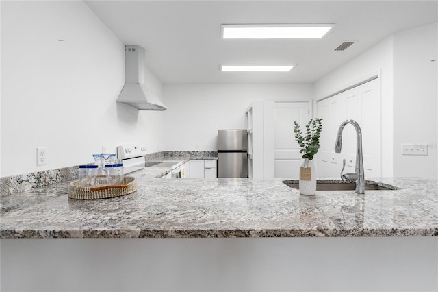 kitchen with wall chimney exhaust hood, sink, white cabinetry, stainless steel refrigerator, and electric stove