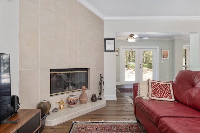 living room featuring french doors, ornamental molding, dark hardwood / wood-style flooring, ceiling fan, and a tiled fireplace