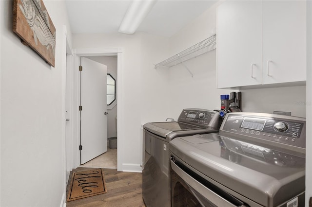 washroom featuring cabinets, washing machine and clothes dryer, and light hardwood / wood-style flooring