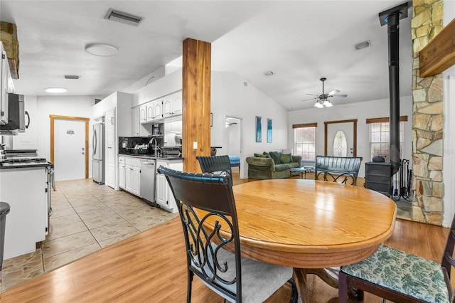 dining room featuring light hardwood / wood-style flooring, vaulted ceiling, ceiling fan, and a wood stove