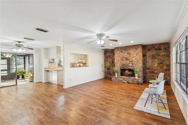 unfurnished living room with ornamental molding, a stone fireplace, a wealth of natural light, and light hardwood / wood-style floors