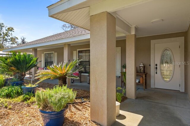 property entrance featuring stucco siding, roof with shingles, and a porch