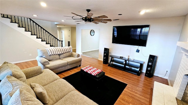 living room with wood-type flooring, ceiling fan, and a fireplace