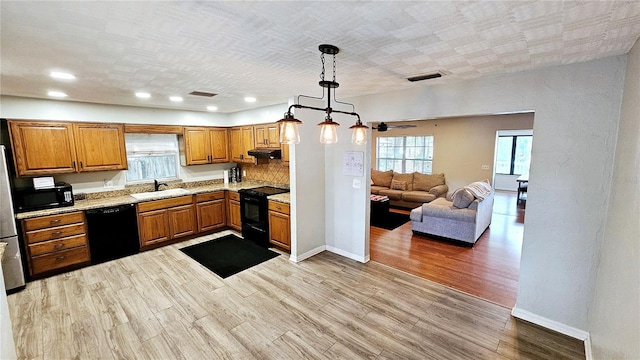 kitchen with sink, light stone counters, black appliances, decorative light fixtures, and light wood-type flooring