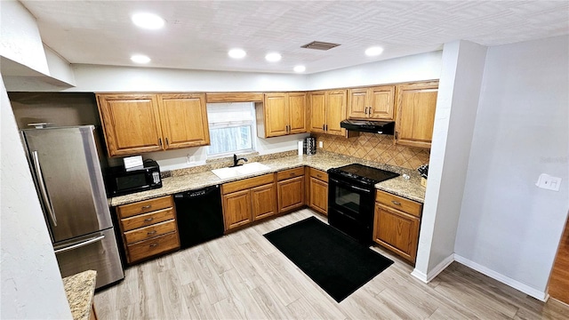 kitchen featuring sink, backsplash, black appliances, light stone countertops, and light hardwood / wood-style flooring