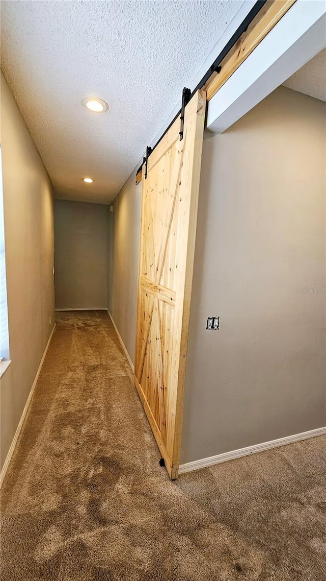 corridor with a barn door, carpet flooring, and a textured ceiling