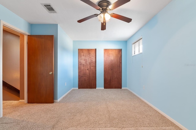 unfurnished bedroom with carpet flooring, two closets, and ceiling fan