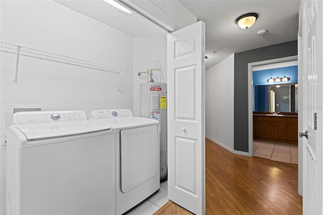 clothes washing area with sink, separate washer and dryer, electric water heater, and light hardwood / wood-style flooring