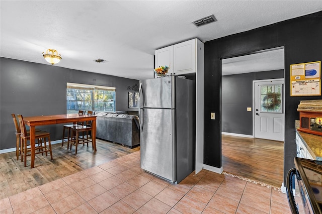 kitchen featuring light tile patterned floors, stainless steel refrigerator, a textured ceiling, white cabinets, and black range oven