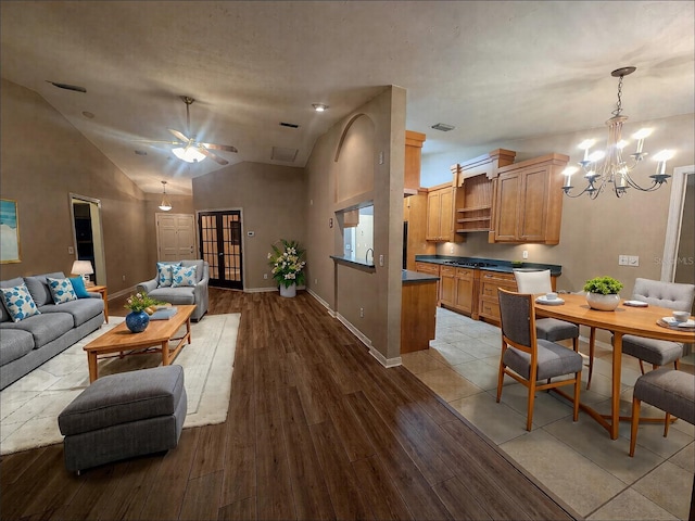 living room with ceiling fan with notable chandelier, light hardwood / wood-style flooring, and high vaulted ceiling