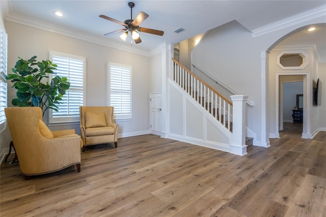 sitting room with stairs, arched walkways, wood finished floors, and ornamental molding