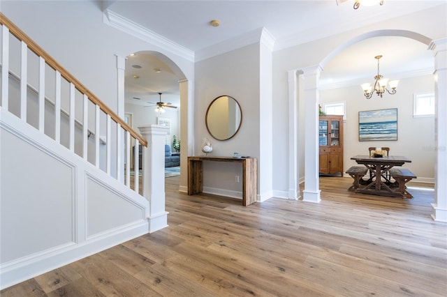 foyer featuring arched walkways, crown molding, light wood-style flooring, and stairs