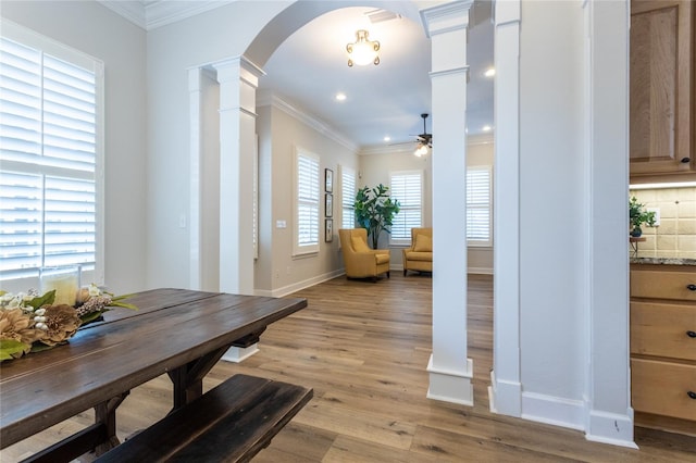 dining room featuring arched walkways, crown molding, decorative columns, light wood-style floors, and ceiling fan