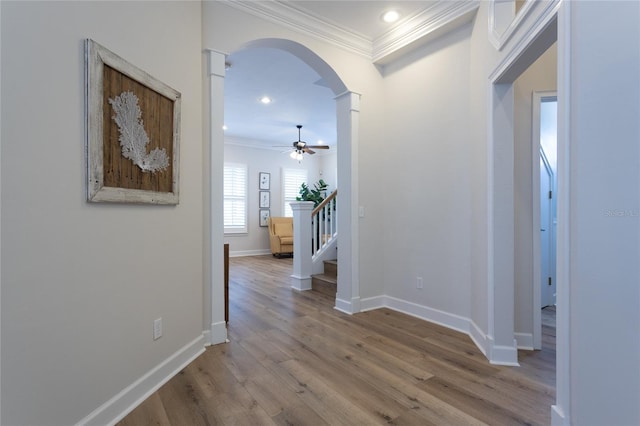 corridor featuring arched walkways, stairway, ornamental molding, wood finished floors, and baseboards