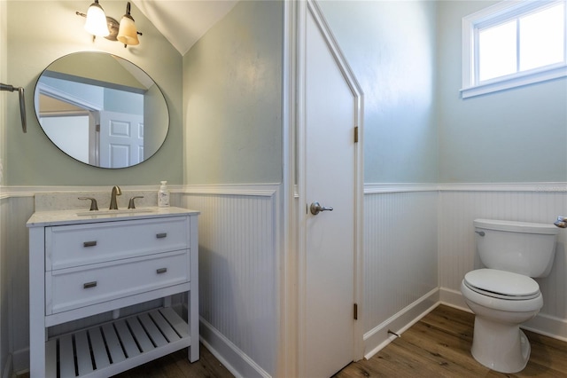 half bathroom with a wainscoted wall, vanity, toilet, and wood finished floors