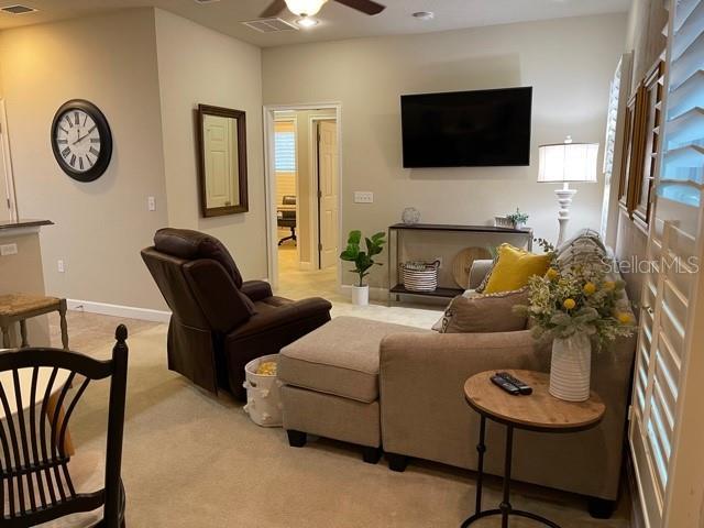 living room featuring ceiling fan, carpet, visible vents, baseboards, and plenty of natural light