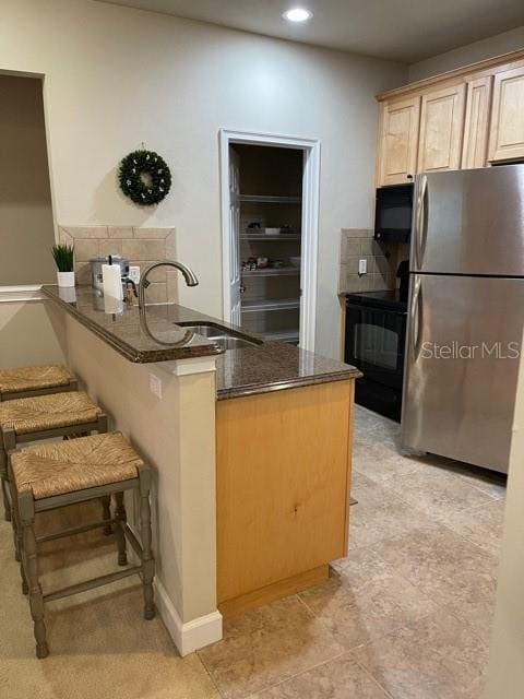 kitchen featuring black microwave, a peninsula, a sink, range, and freestanding refrigerator