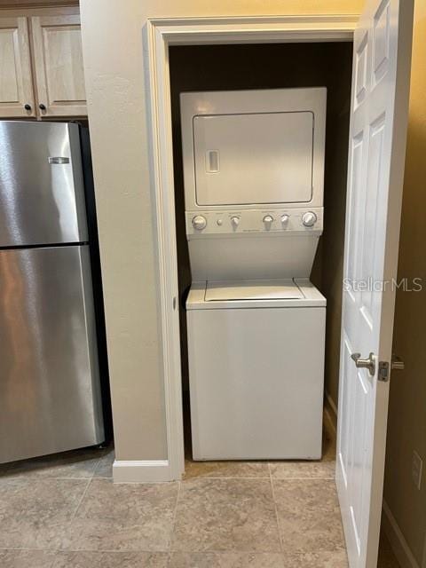 clothes washing area featuring baseboards, laundry area, light tile patterned floors, and stacked washer / drying machine