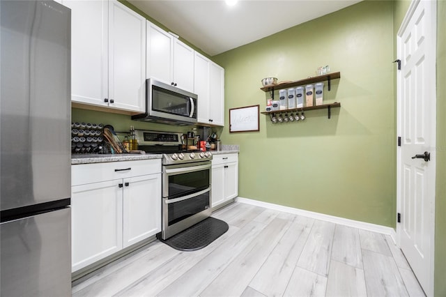 kitchen featuring light stone counters, appliances with stainless steel finishes, light hardwood / wood-style floors, and white cabinets