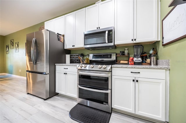 kitchen featuring stainless steel appliances, light stone countertops, light hardwood / wood-style flooring, and white cabinets