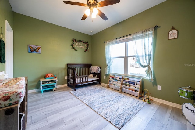 bedroom with light hardwood / wood-style floors, a nursery area, and ceiling fan