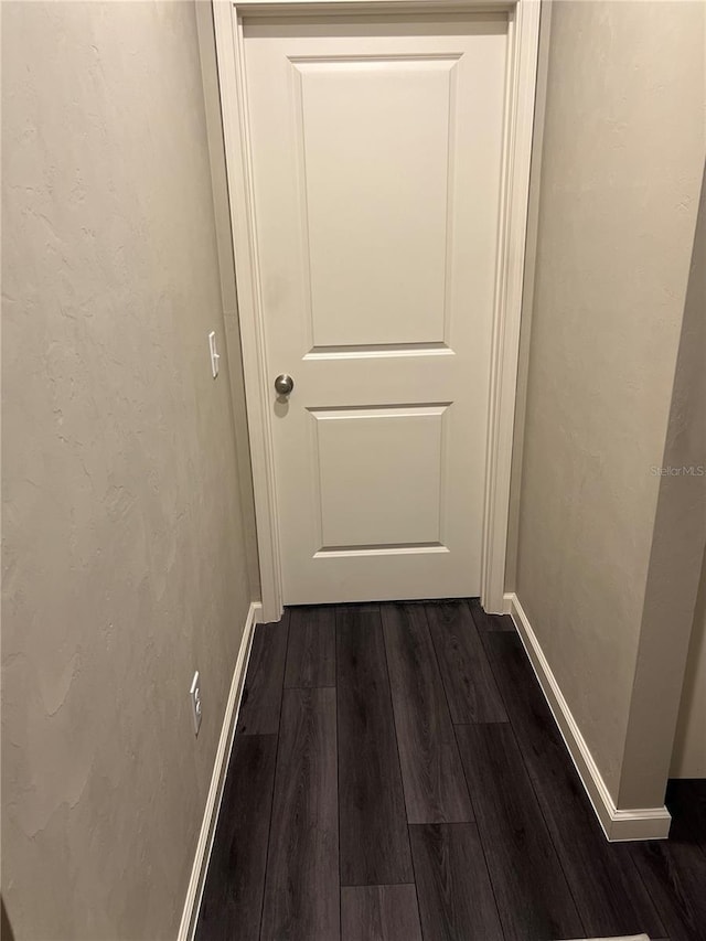 corridor with dark wood-type flooring, a textured wall, and baseboards