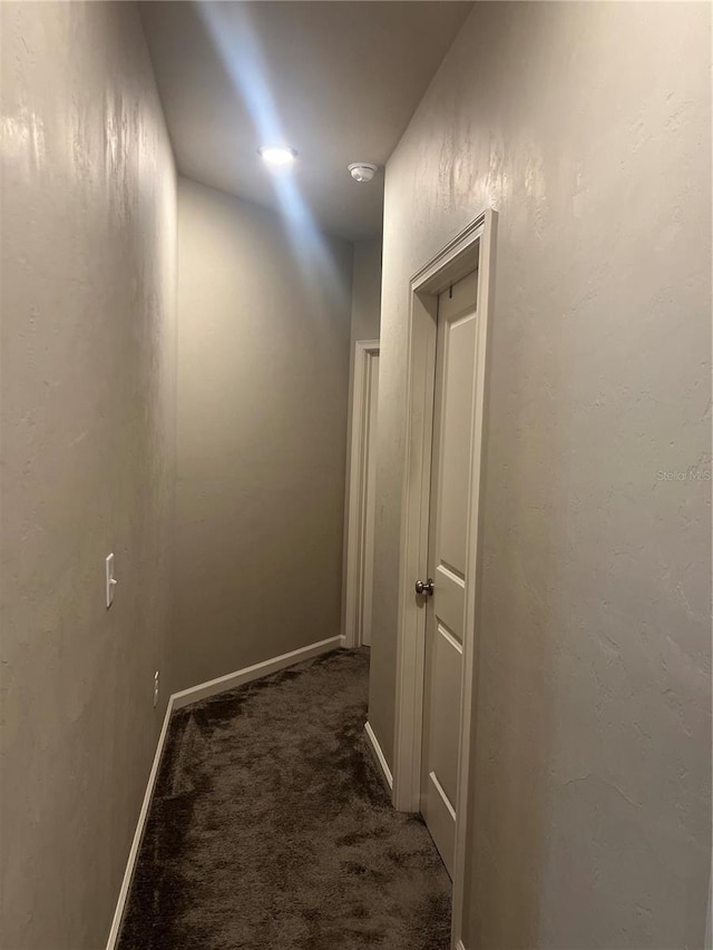 hall with baseboards, dark colored carpet, and a textured wall