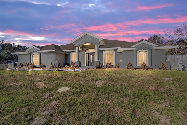 single story home with stucco siding, fence, and a lawn