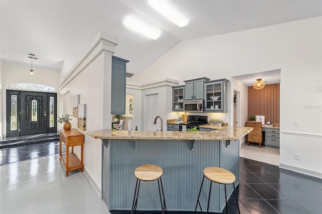 kitchen featuring stainless steel microwave, electric range, light stone countertops, a peninsula, and a kitchen breakfast bar