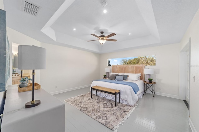 bedroom with a ceiling fan, visible vents, a tray ceiling, and baseboards