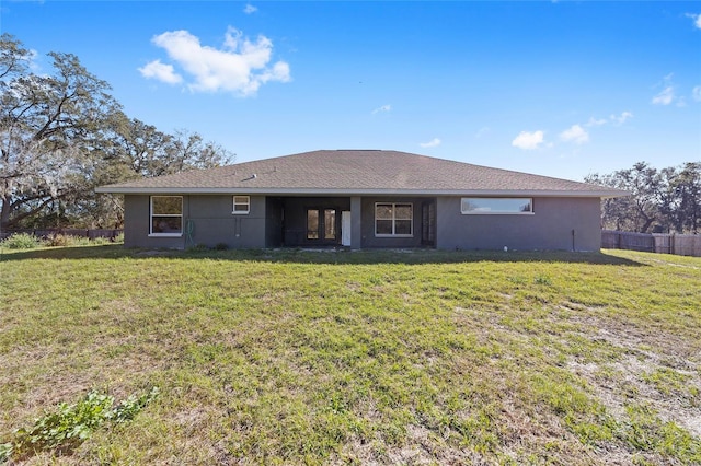 rear view of house with a yard, fence, and stucco siding