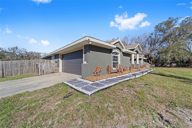 view of side of property with a lawn, concrete driveway, an attached garage, fence, and stucco siding