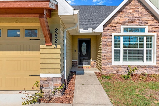 view of exterior entry featuring an attached garage, stone siding, and a shingled roof