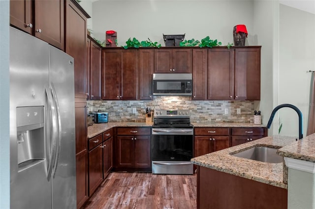 kitchen with wood finished floors, a sink, appliances with stainless steel finishes, backsplash, and light stone countertops