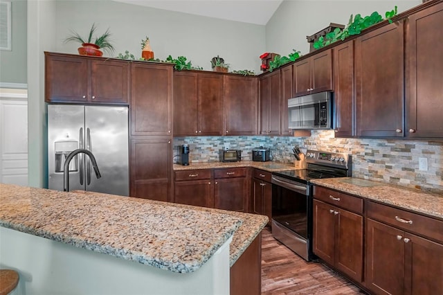 kitchen featuring stainless steel appliances, dark brown cabinets, and light stone countertops