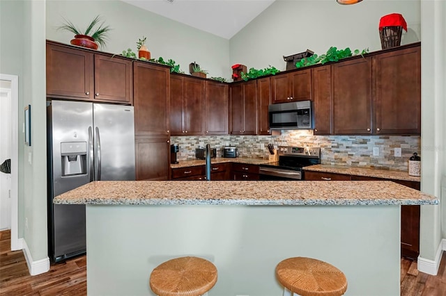 kitchen with stainless steel appliances, a breakfast bar, a kitchen island with sink, and light stone countertops