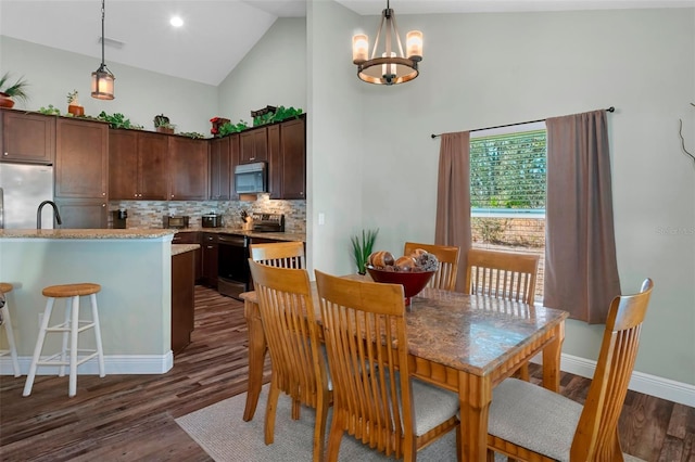 dining space featuring baseboards, visible vents, dark wood finished floors, a chandelier, and high vaulted ceiling