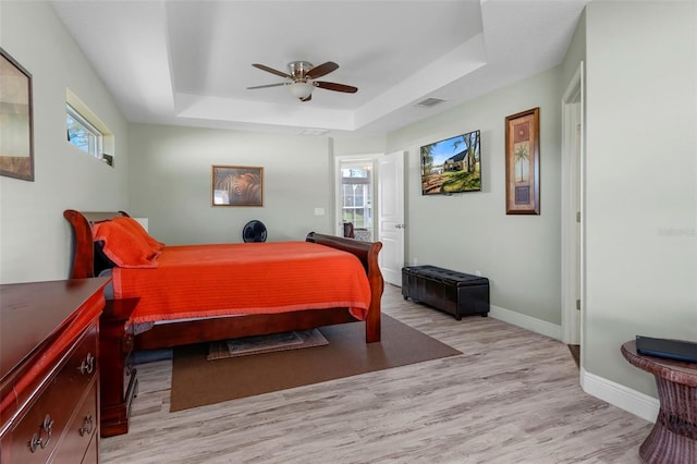 bedroom featuring visible vents, multiple windows, a tray ceiling, and light wood-style flooring