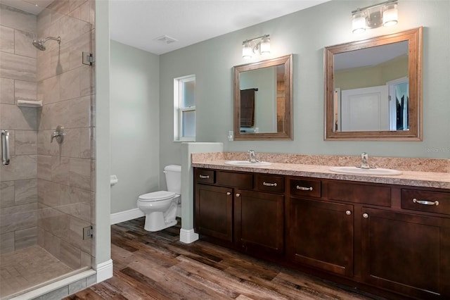 bathroom featuring double vanity, a stall shower, toilet, wood finished floors, and a sink