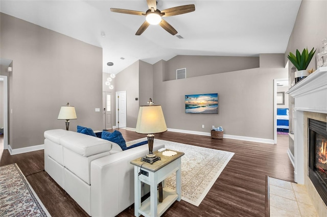 living room with vaulted ceiling, wood finished floors, baseboards, and a tile fireplace