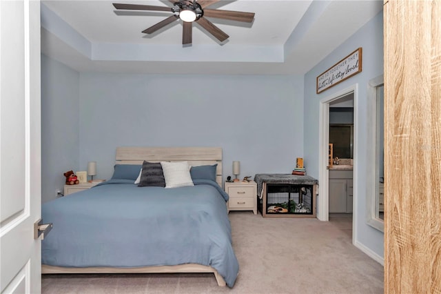 bedroom featuring ceiling fan, a tray ceiling, and light carpet