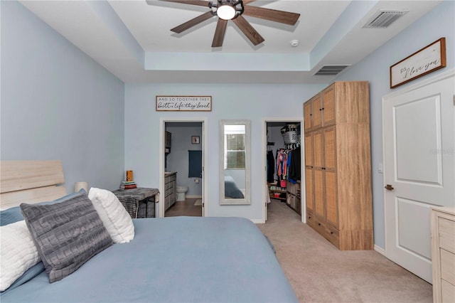 carpeted bedroom featuring ceiling fan, connected bathroom, a tray ceiling, a walk in closet, and a closet