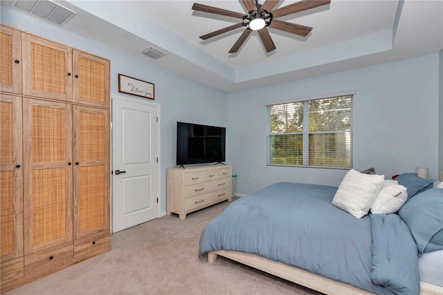 bedroom featuring a raised ceiling, light colored carpet, and ceiling fan