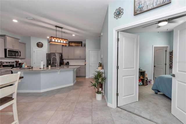 kitchen featuring stainless steel appliances, a center island with sink, gray cabinetry, and hanging light fixtures