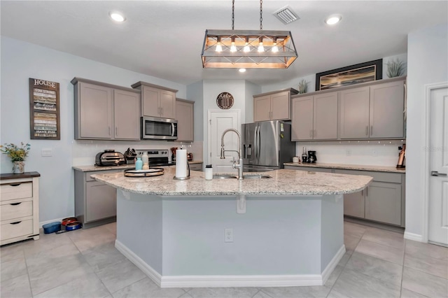 kitchen featuring light stone counters, decorative light fixtures, stainless steel appliances, and a center island with sink