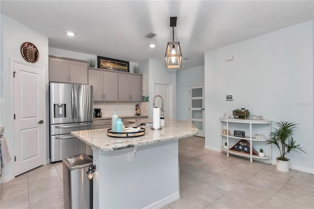 kitchen featuring gray cabinetry, decorative light fixtures, stainless steel fridge with ice dispenser, light stone countertops, and a kitchen island with sink