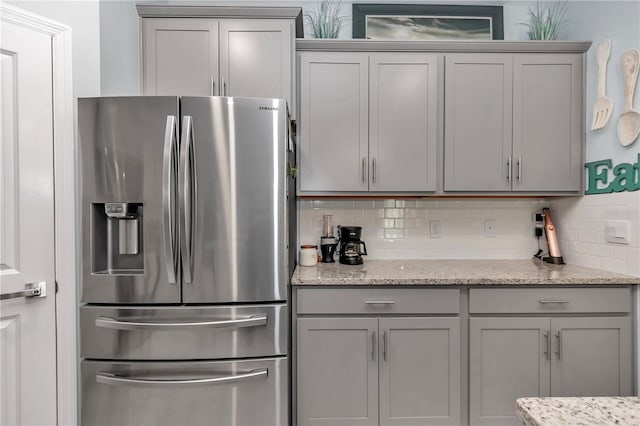 kitchen with gray cabinetry, stainless steel fridge with ice dispenser, backsplash, and light stone countertops