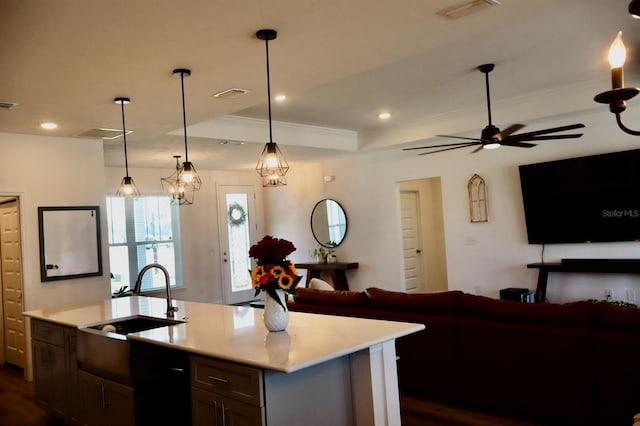 kitchen featuring pendant lighting, dishwasher, an island with sink, sink, and a tray ceiling